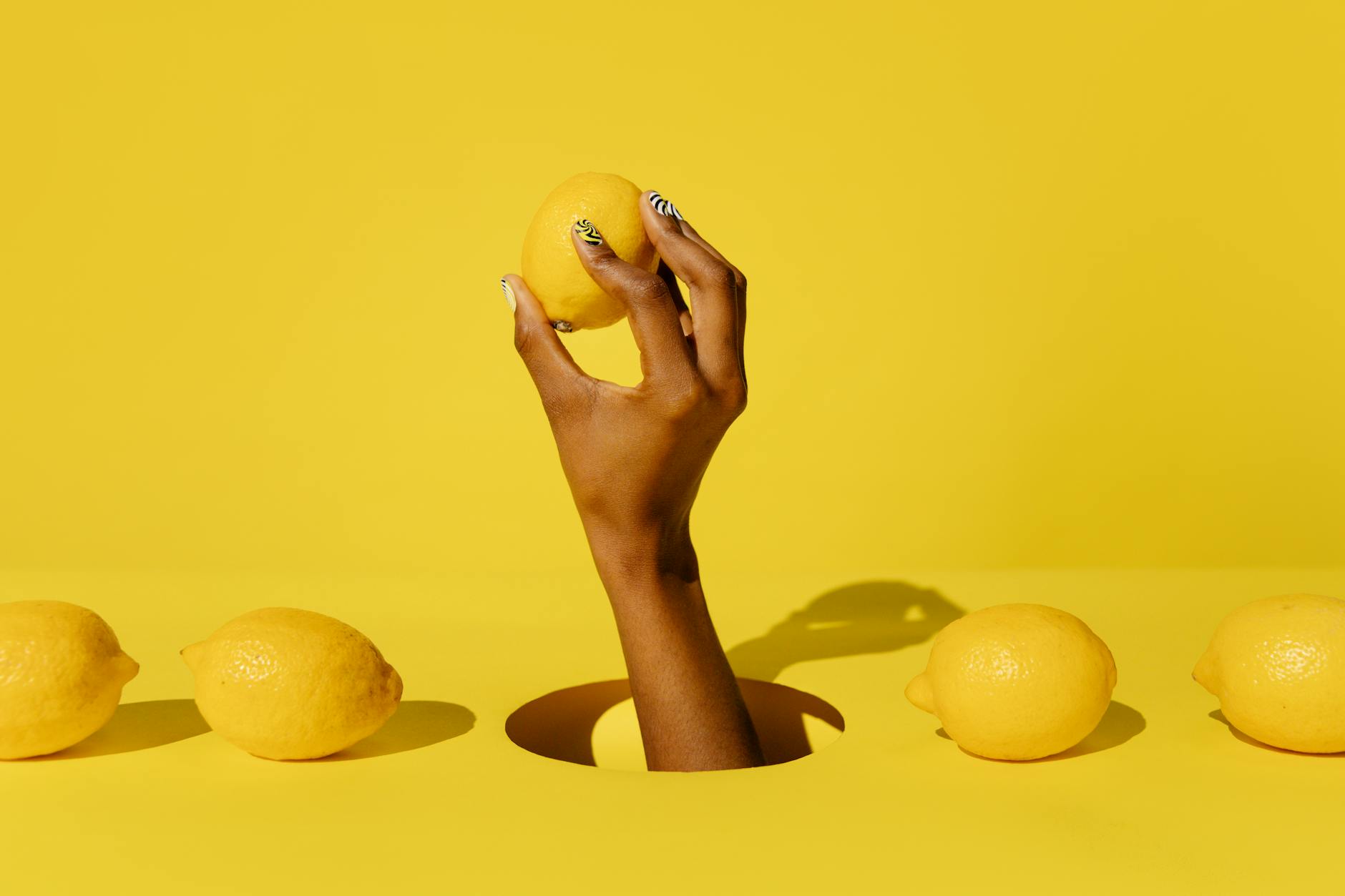 Hand holding a fresh lemon against a vibrant yellow background, symbolizing the Lemon Vibrator brand