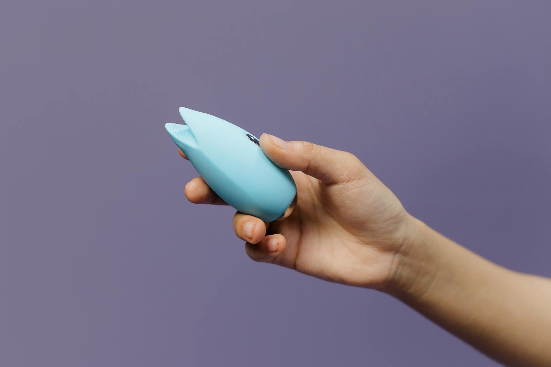 Woman holding blue and pink silicone vibrators in a thoughtful moment of self-discovery