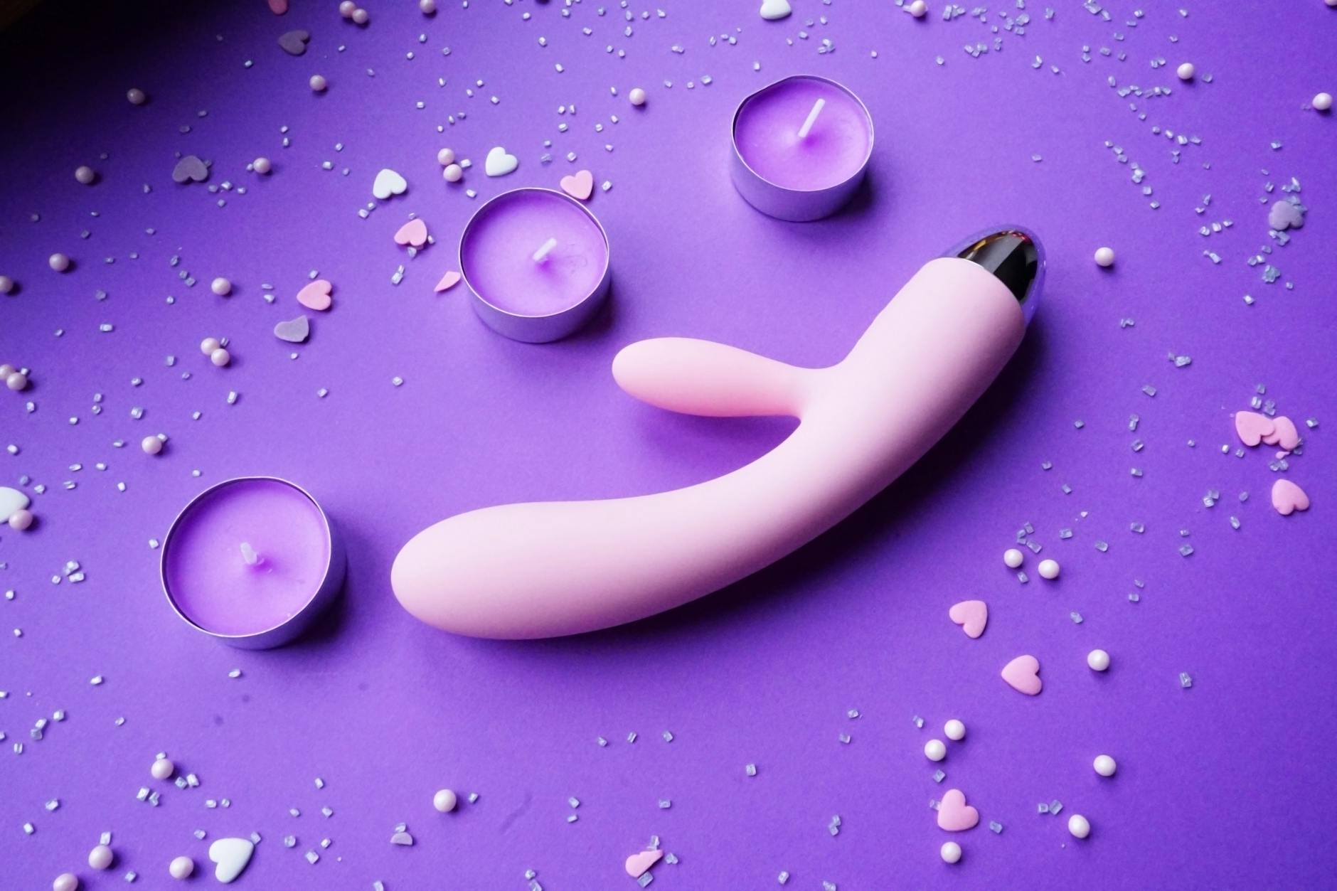 Pink lemon-shaped vibrator displayed on purple fabric with hearts and romantic lighting